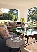 Seating area on sunny roofed terrace with sofa, wicker armchairs and coffee table on Oriental rug with stool used as side table in foreground