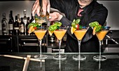 Barkeeper giesst Cocktails aus Shaker in Cocktailgläser
