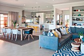 Blue corner sofa with scatter cushions and patterned rug in front of dining area with shell chairs and open-plan kitchen