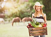 Junge Frau trägt Holzkiste mit frischen Gartengemüse