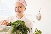 Köchin in Arbeitskleidung trägt Gemüsekiste