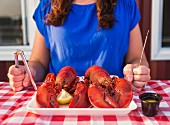 A woman holding lobster cutlery sitting in front of a platter of cooked lobster