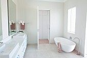 Designer bathtub with floor-mounted tap and long washstand with countertop sinks in minimalist white bathroom