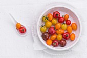 Various different coloured tomatoes in a porcelain bowl and on a spoon (seen from above)
