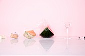 A champagne cork, melon wedges and a broken glass against a pink background