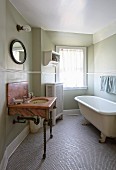 Marble washstand on wrought iron legs and free-standing vintage bathtub on mosaic-tiled floor