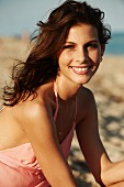 A young woman on a beach wearing a pink summer dress