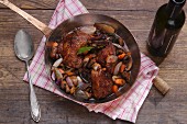 Coq au vin in a copper pan on a wooden surface