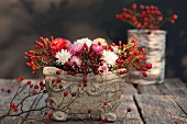 Autumnal flower arrangement with rose hips in stone bowl on wooden table
