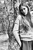 A young woman wearing a cardigan and a skirt leaning on a tree (black-and-white shot)