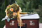 Festlicher Blumenstrauss aus apricotfarbenen Rosen und Hortensien mit Schleife, auf Vintage Koffer