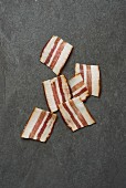 Six rashers of smoky bacon on a grey surface (seen from above)