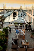 Woman and man on Mediterranean terrace with view of large yachting marina in background