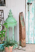 Arrangement mit nostalgischem Laternen-Windlicht und bedrucktem Holzbalkenstück vor verwitterter, türkisfarbener Vintagetür