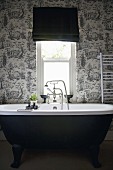 Black, free-standing bathtub against black and white toile de jouy wallpaper