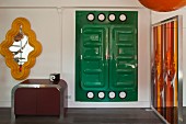 Postmodernes Kleinmöbel, orangerotes Kunstobjekt, gelber Wandspiegel und grüner Kunststoff-Wandschrank; Pop Art Ambiente