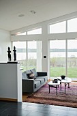 Nest of curved coffee tables and grey three-seater sofa on rug next to glass wall