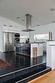 Stainless steel extractor hood above island counter in open-plan designer kitchen