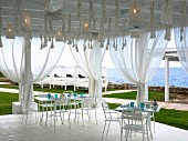 Set table on white wooden terrace with curtains and sea view