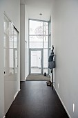 Schmaler, hoher Gang mit schwarzen Fliesenboden, seitlich eingebauter Schrank mit weissen, Schiebetüren, verglaster Hauseingang im Hintergrund