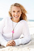 A young blonde woman by the sea wearing a light knitted jumper