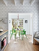 Floor-to-ceiling white wall tiles in kitchen and open doorway with view of dining area with green designer chairs