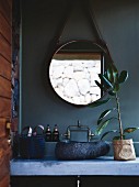Beton-Waschtisch mit Waschschüssel aus Stein darüber runder Spiegel an petrolfarbener Wand