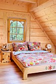 Double bed with floral bed linen in attic room with pale wooden cladding