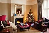 Geschmückter Weihnachtsbaum in viktorianischem Wohnzimmer mit gemütlichen Polstermöbeln vor Kaminfeuer