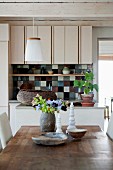 View across wooden table to kitchen counter with multicoloured ceramic-tiled splashback