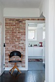 Retro chair with black leather cover against brick wall in hallway with view of white kitchen counter through open door