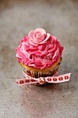 A vanilla cupcake with pink mascarpone cream and a decorative flower