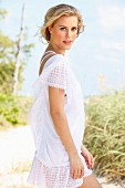 A young blonde woman on a beach wearing a white lace dress