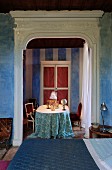 Bed in front of open doorway with white, carved wooden frame and view of table in Mediterranean parlour with vintage ambiance