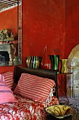Wohnraum in Rot mit nostalgischem Charme, Kissen rot-weiss gestreift auf Tagesliege und farbige Vasensammlung auf Beistelltisch