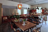 Grosszügige Küche mit Essplatz im Vintagestil, im Hintergrund Kücheninsel unter Pendelleuchten und Buffettisch unter moderner Edelstahlverkleidung