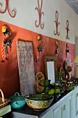 Green ceramic crockery and fruit on sideboard against red-brown wall with Indian-style decorations