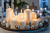 Lit white pillar candles of various sizes and silver baubles on tray