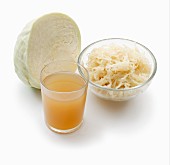 White cabbage, sauerkraut and a glass of sauerkraut juice on a white surface