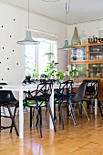 Black designer chairs around white table below pendant lamps in Scandinavian-style dining room