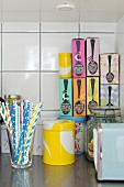 Colourful drinking straws, yellow tin and stack of colourful boxes of tea on kitchen worksurface