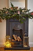 Fairy lights in large glass jar and lantern on hearth of cast iron fireplace with festive arrangement on mantelpiece