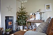 Decorated Christmas tree between wood-burning stove and gifts on console table in rustic living room