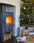 Gifts below Christmas tree next to cast iron log burner in fireplace
