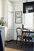 Essplatz in der Küche am Fenster mit schwarzen Bistrostühle um Holztisch, seitlich eingebaute weiße Kühlschrankkombination