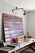 Abstract red and black artwork on rustic wooden table under wall-mounted lamp