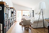 Designer standard lamp next to white loose-covered sofa and bookcase with TV in centre in living room