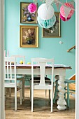White wooden chairs and vintage table in decorated dining room with gilt-framed floral pictures on blue wall