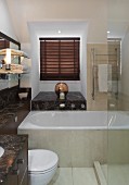 Dunkelfarbene Marmor-Waschtischplatte mit Ablageflächen, weiße Badewanne und Glas-Duschabtrennung im Bad