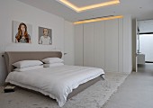 Graues Doppelbett mit gepolstertem Kopfteil und weißer Einbauschrank in modernem Schlafzimmer mit indirekter Beleuchtung
